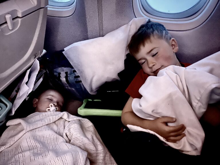 Baby and toddler peacefully sleeping on an airplane during a long-haul flight, illustrating successful sleep routines while traveling.
